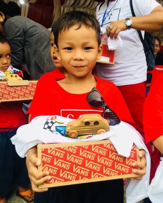 Cambodian boy holding shoe box with toy car sitting on top.
